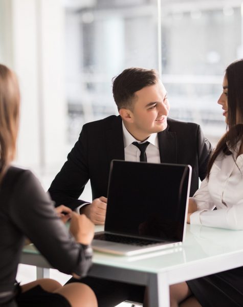 Confident young woman explain some details of document and pointing it with smile while sitting together with young couple at the desk in office